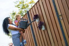 Vrouw en kind geven plantjes water die aan een hout met beton schutting hangen