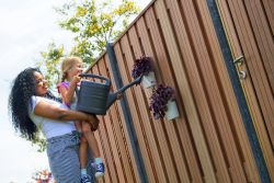 Vrouw en kind geven plantjes water die aan een hout met beton schutting hangen